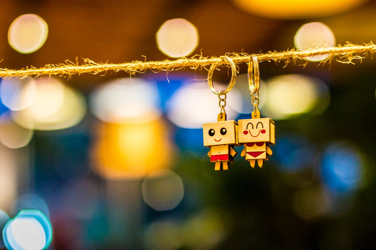 Charming wooden cartoon keychain dolls hanging with vibrant bokeh lights in the background, creating a playful and colorful ambiance.