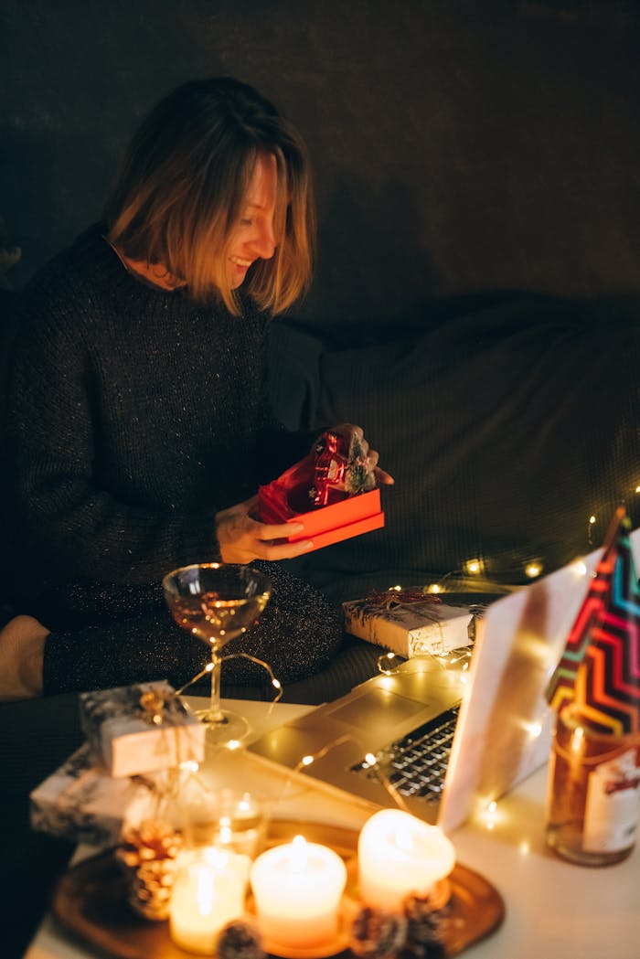 Woman enjoying a festive online unboxing experience with candles and decorations.