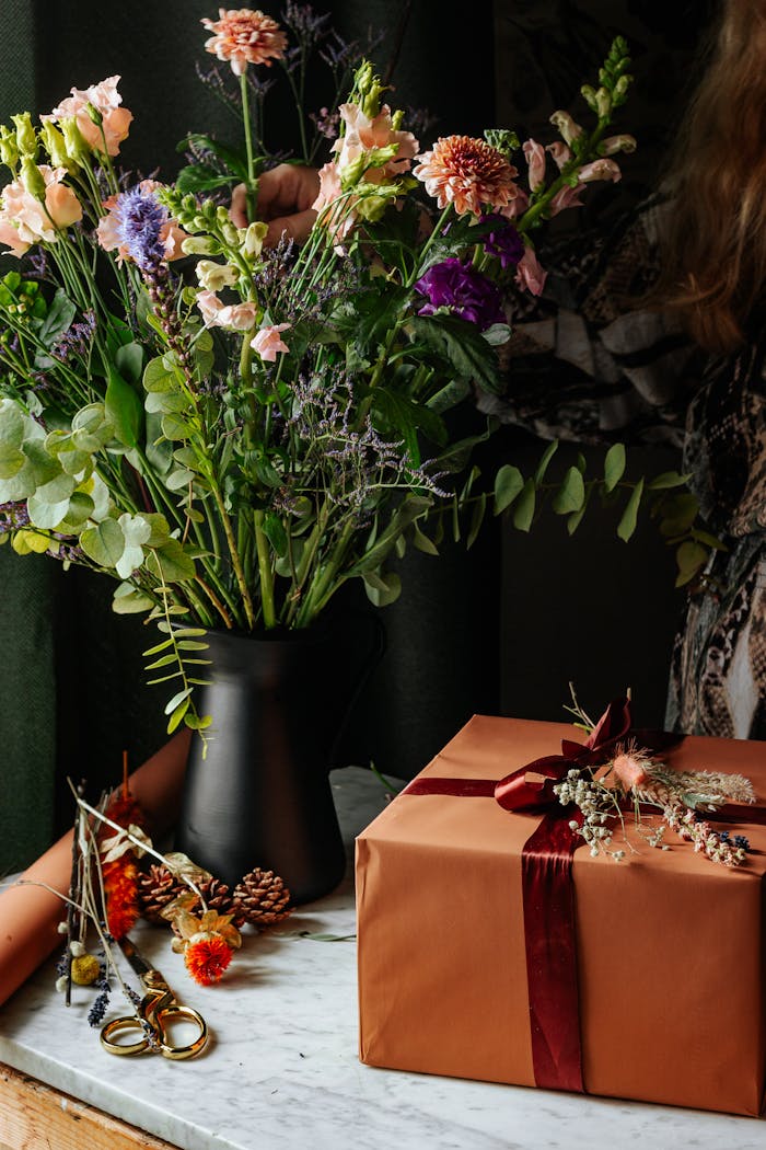 Stylish floral bouquet in a black vase with a wrapped gift on marble. Perfect for celebrations and decor.